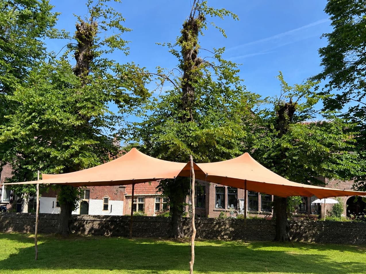 Oranje stretchtent op een grasveld bij een monumentaal pand
